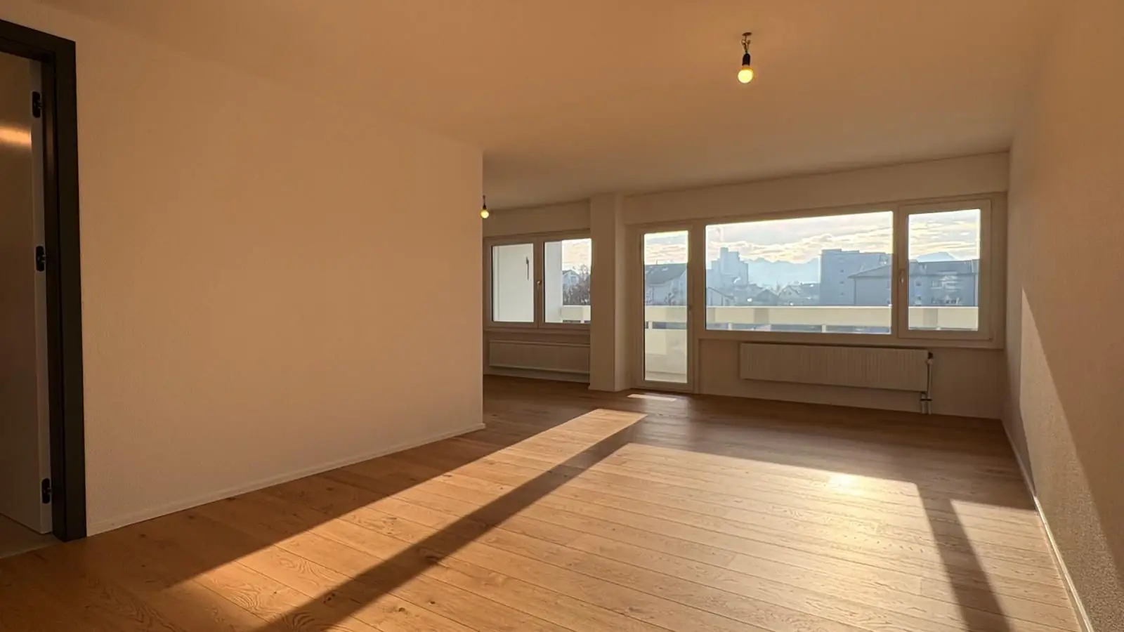 Heller Wohnraum mit Fensterfront, Balkontür und Eichenparkett – Umbau in Emmen
