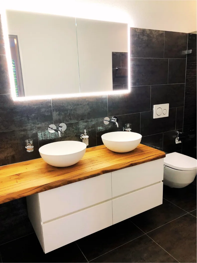 Badezimmer mit Doppellavabo auf Holzabdeckung und beleuchtetem Spiegel – Neubauwohnung Zürich