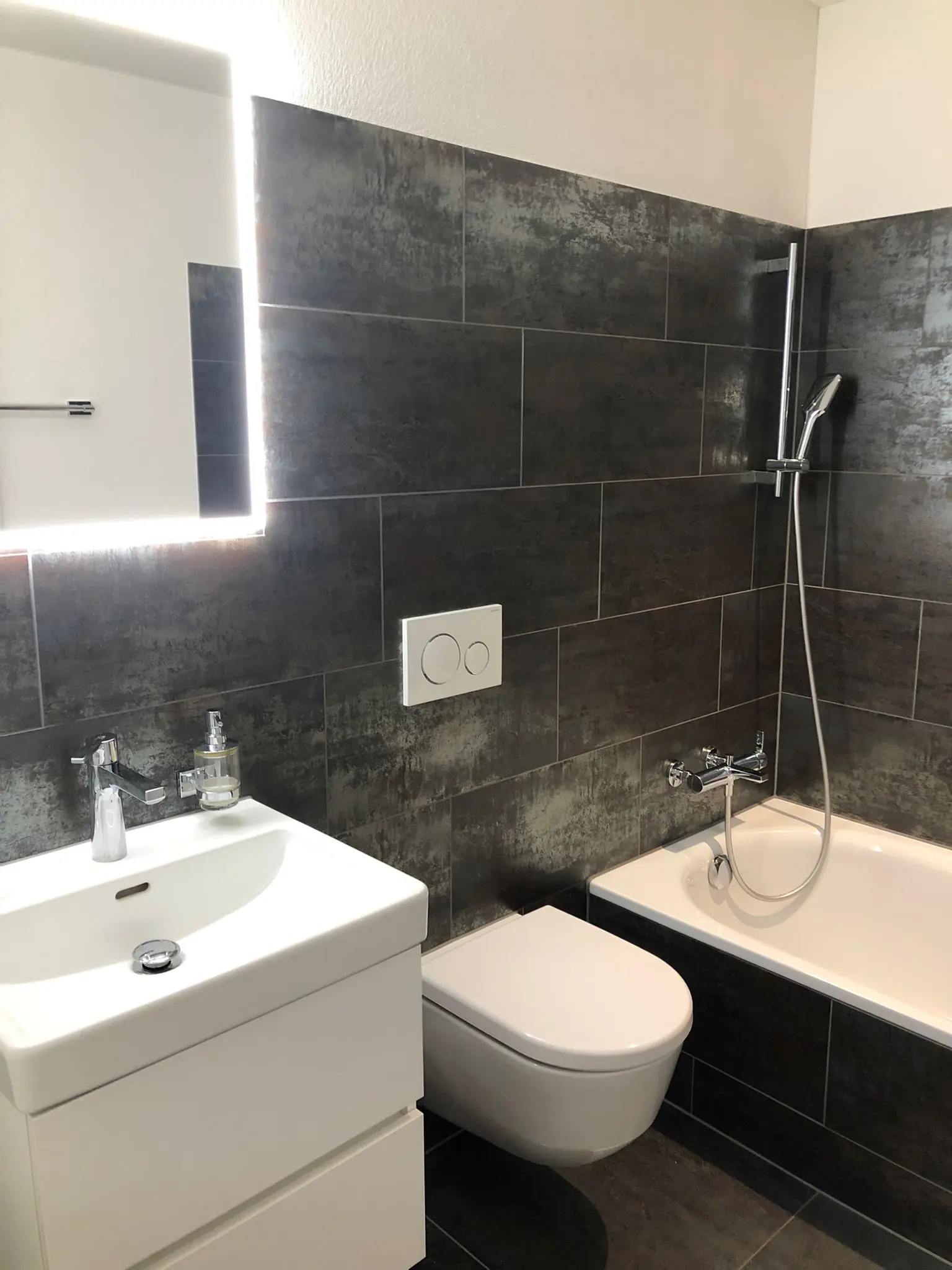 Badezimmer mit Badewanne, Lavabo und beleuchtetem Spiegel – Neubauwohnung Zürich