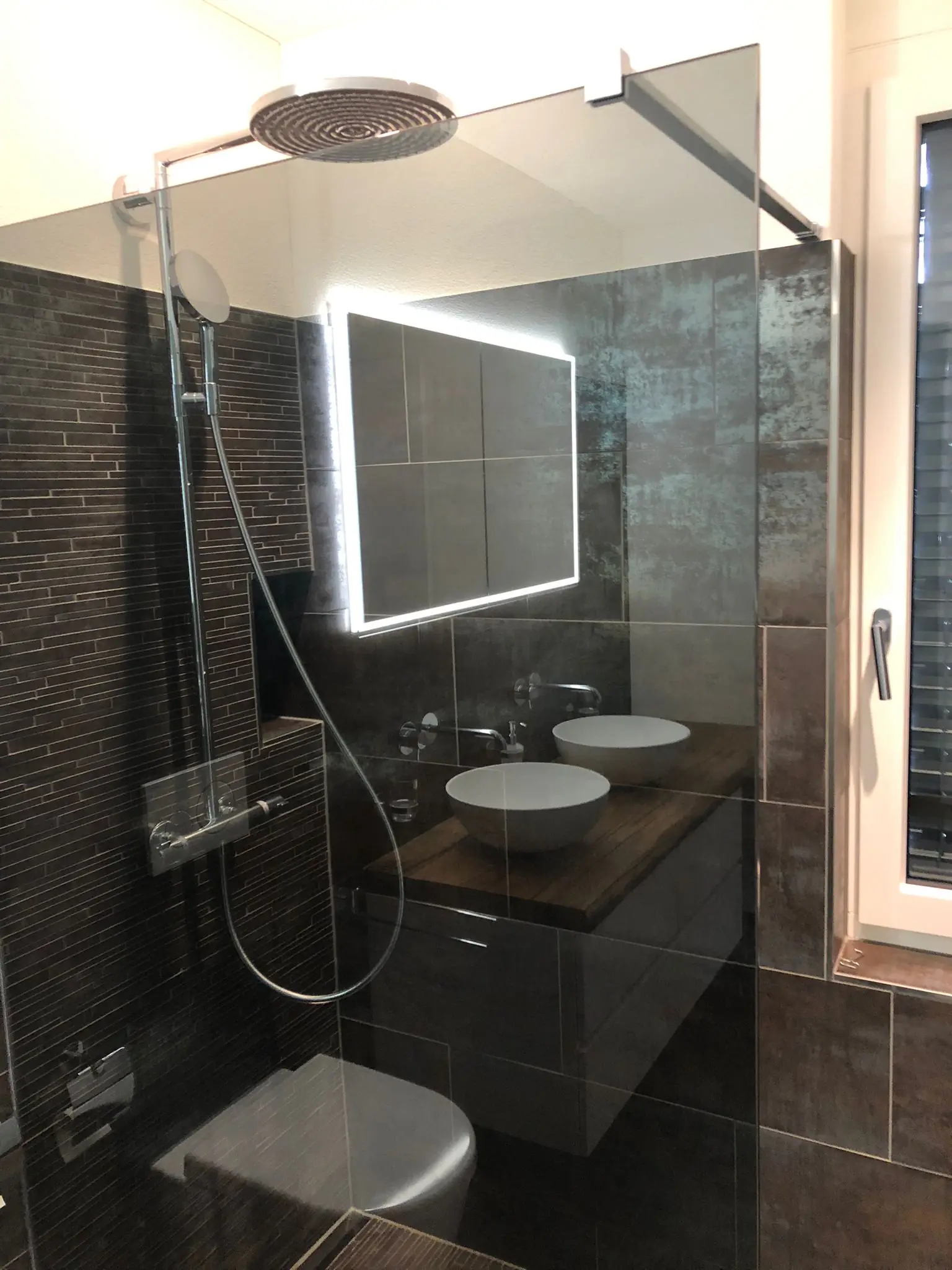 Walk-in-Regendusche mit Glaswand und dunklen Platten – Neubauwohnung Zürich