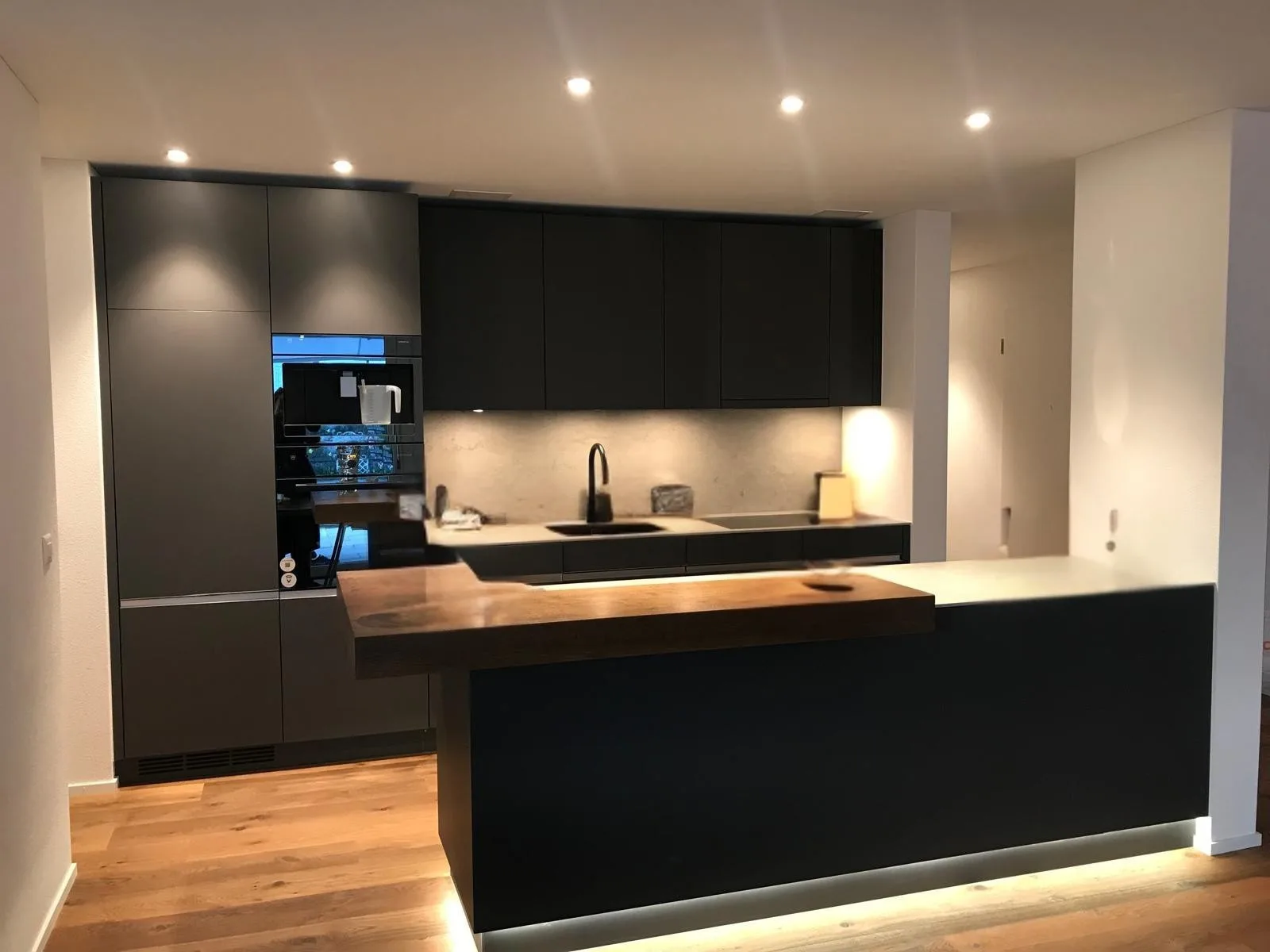 Dunkle Designküche mit Holztheke und indirekter Beleuchtung – Neubauwohnung in Zürich, ARTIAS Group