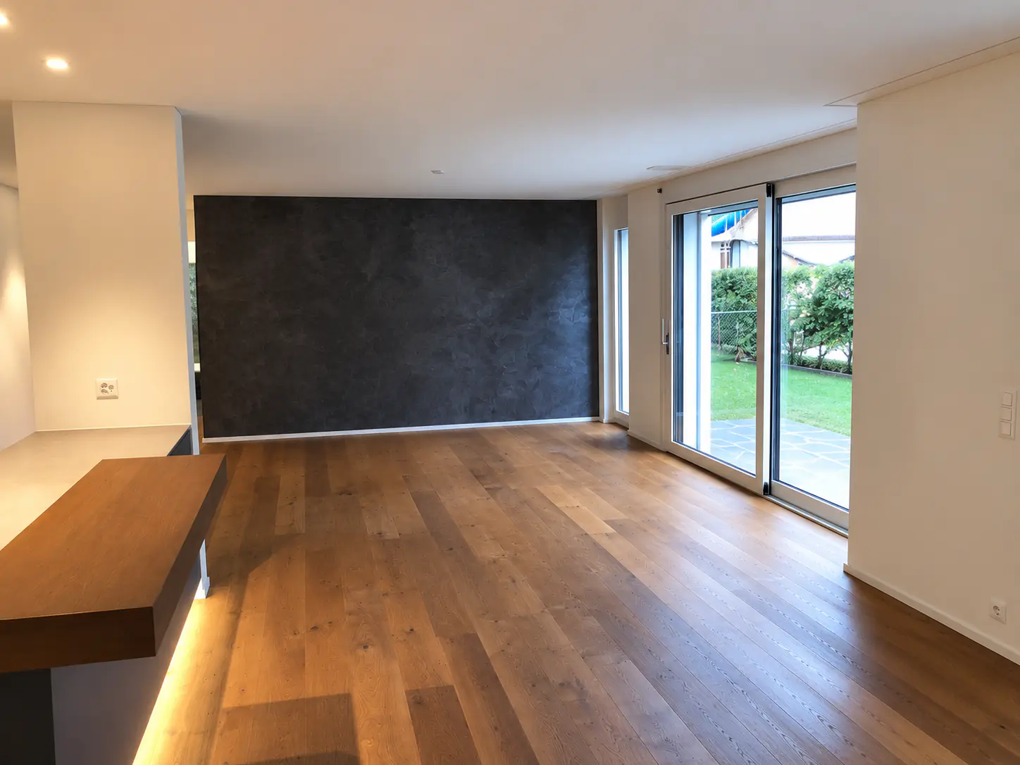 Leerer Wohnraum mit dunkler Akzentwand und Gartenblick – Neubauwohnung Zürich