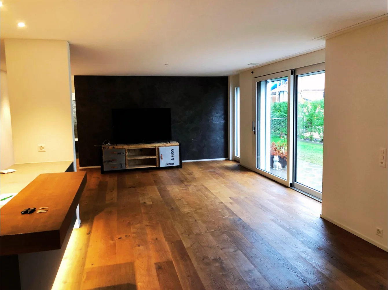 Wohnzimmer mit dunkler Akzentwand und Gartenblick – Neubauwohnung Zürich