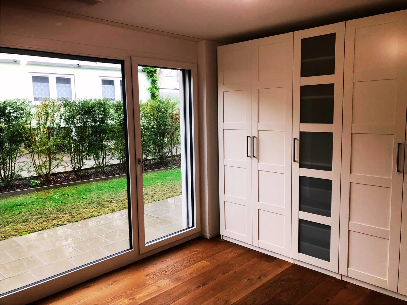 Zimmer mit weissen Einbauschränken und Gartenzugang – Neubauwohnung Zürich